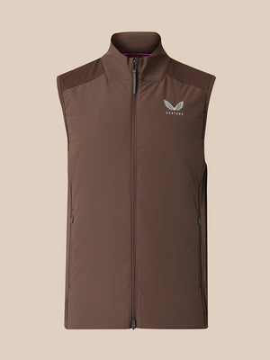 A sleeveless zip-front vest in dark brown with a stand collar and a small white wing logo on the left chest, shown against a plain beige background.
