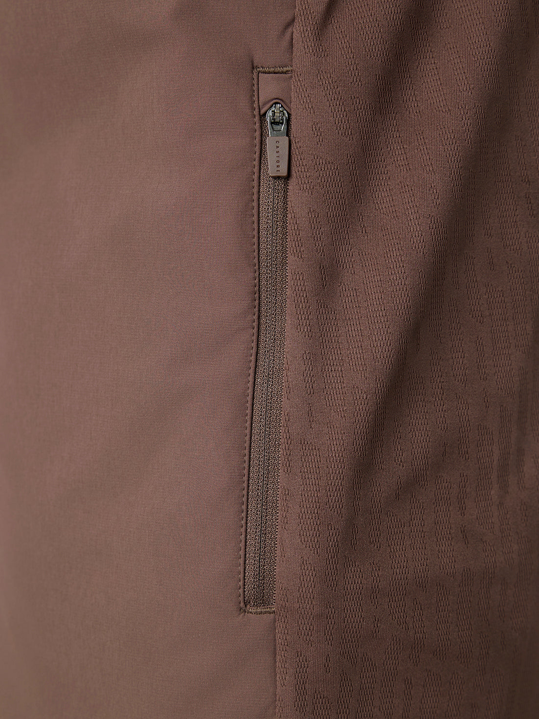 Close-up of a brown fabric jacket showing a vertical zippered pocket with a silver zipper pull.