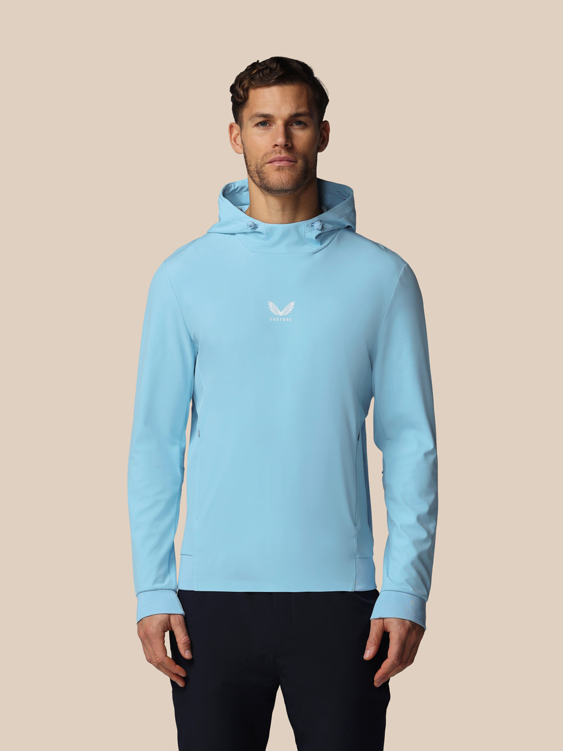 Man wearing a light blue hoodie with a logo on a beige background
