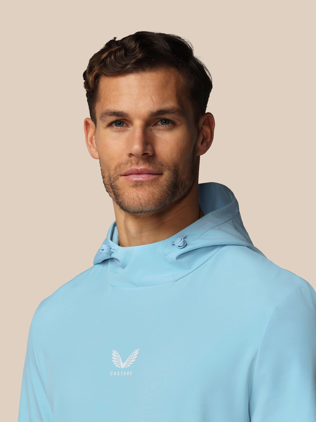 Man wearing a light blue hoodie with a logo on a beige background