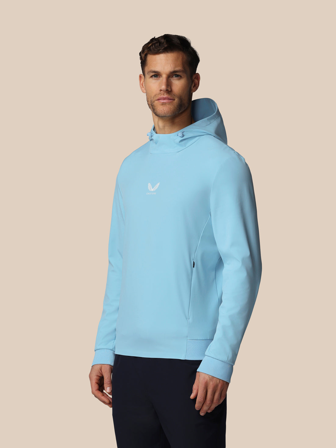 Man wearing a light blue hoodie with a logo on a beige background