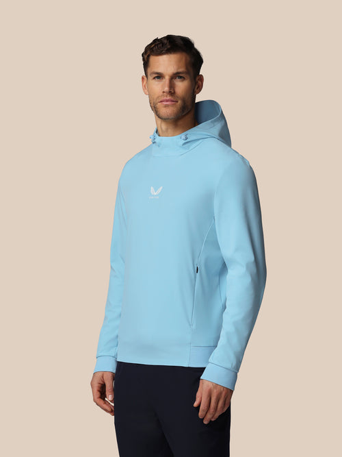 Man wearing a light blue hoodie with a logo on a beige background
