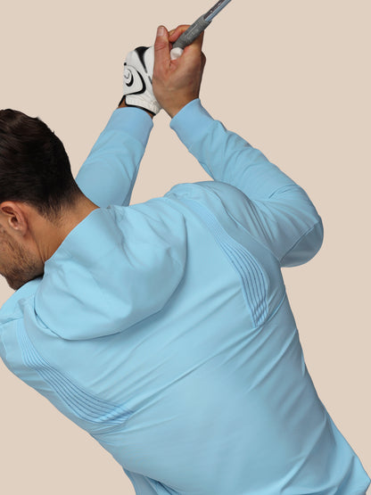 Man in light blue outfit swinging a golf club against a beige background