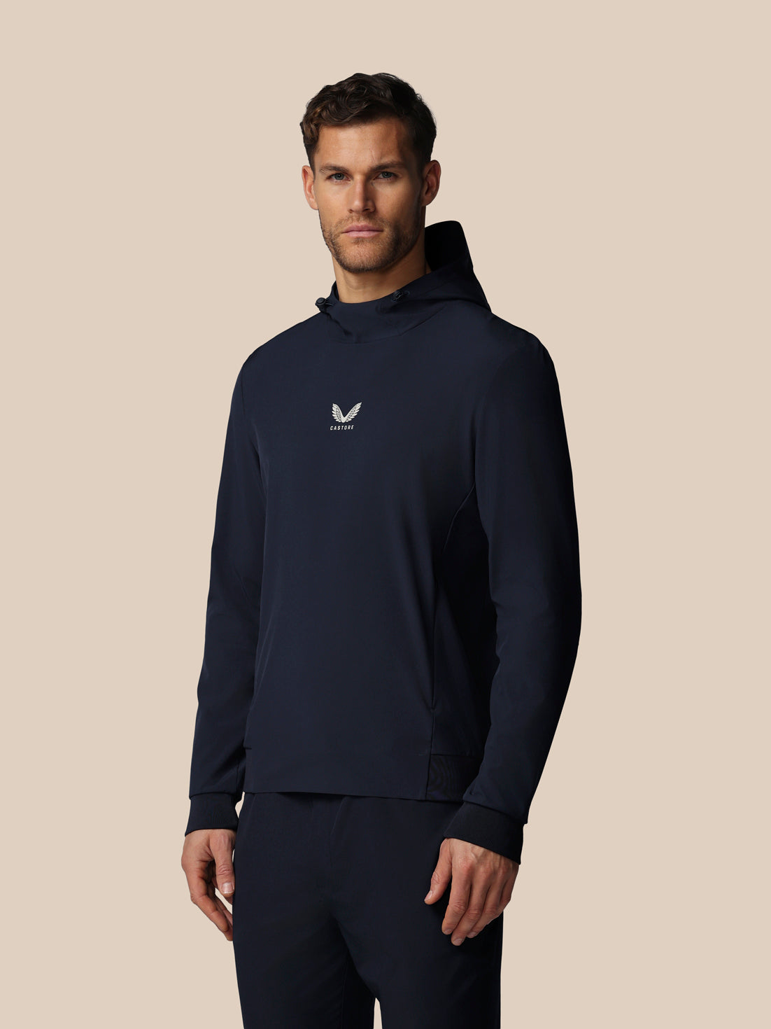Man wearing a navy hoodie with a logo on a beige background