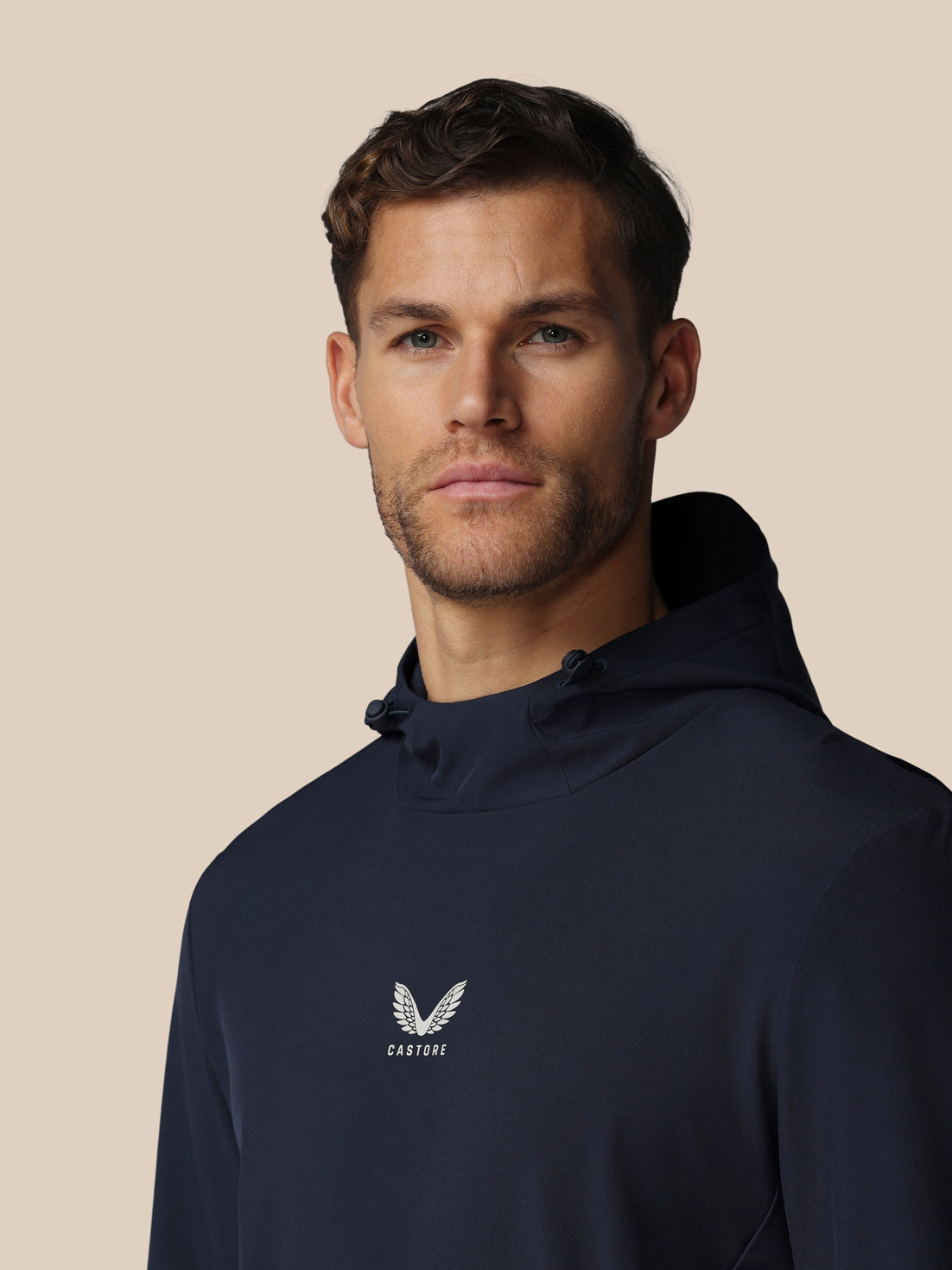 Man wearing a navy hoodie with a logo on a beige background