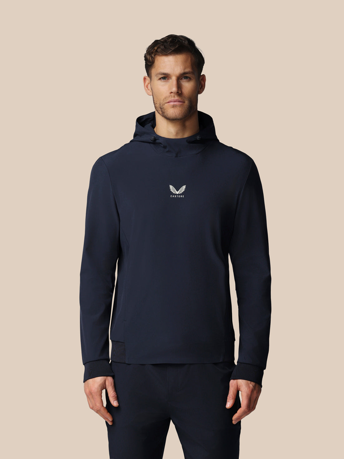 Man wearing a navy hoodie with a logo on a beige background