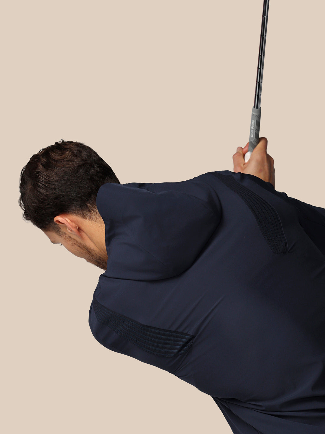 Man in a dark suit holding a golf club against a beige background
