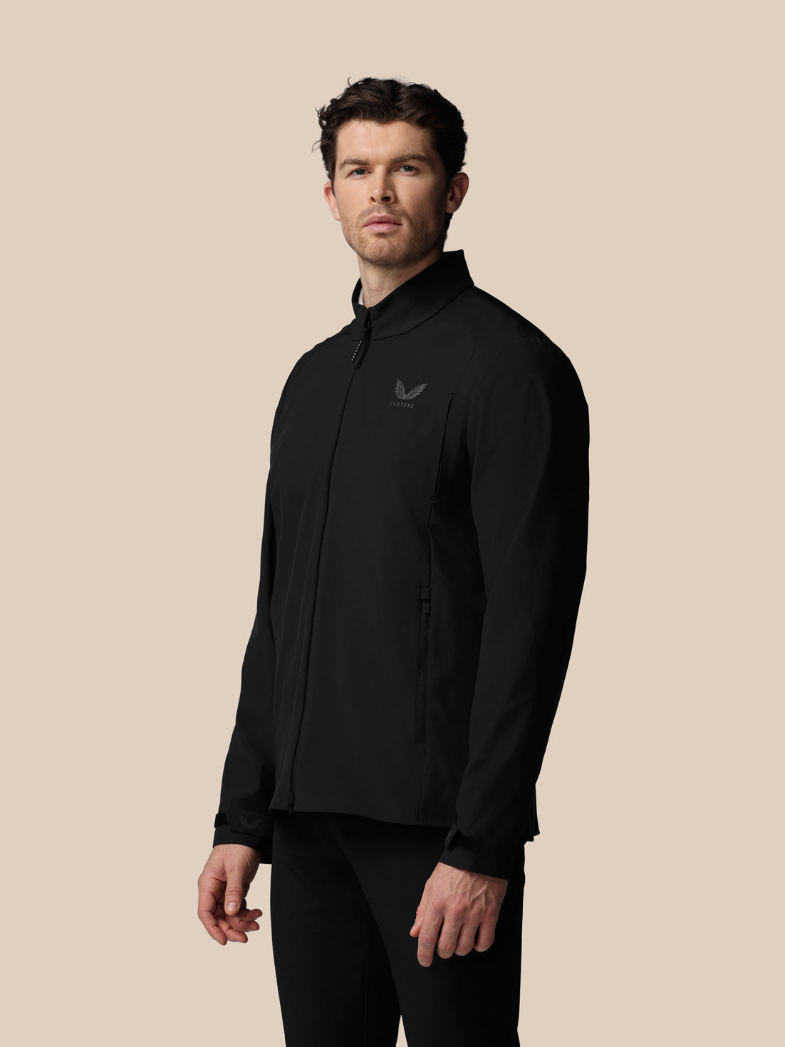 Man wearing a black jacket with a logo on a beige background