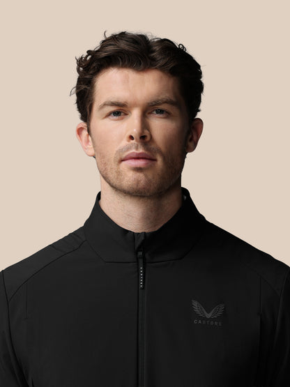 Man wearing a black jacket with a logo on a beige background
