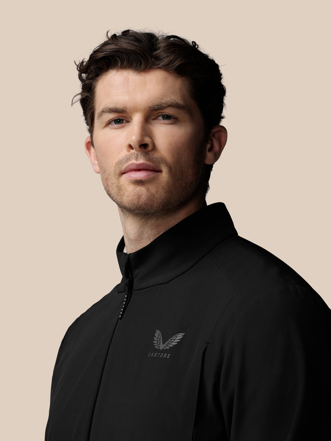 Man wearing a black Castore jacket against a beige background