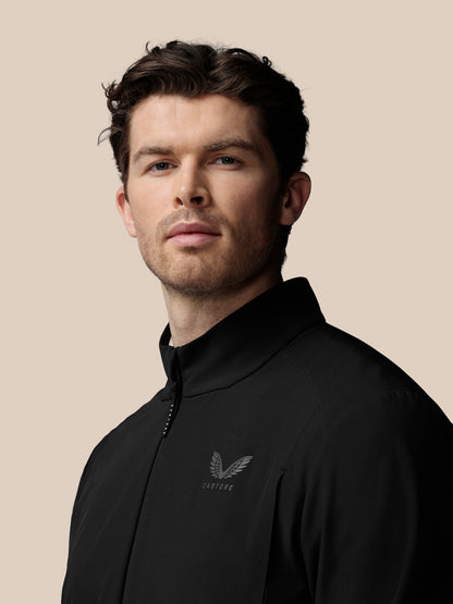 Man wearing a black Castore jacket against a beige background