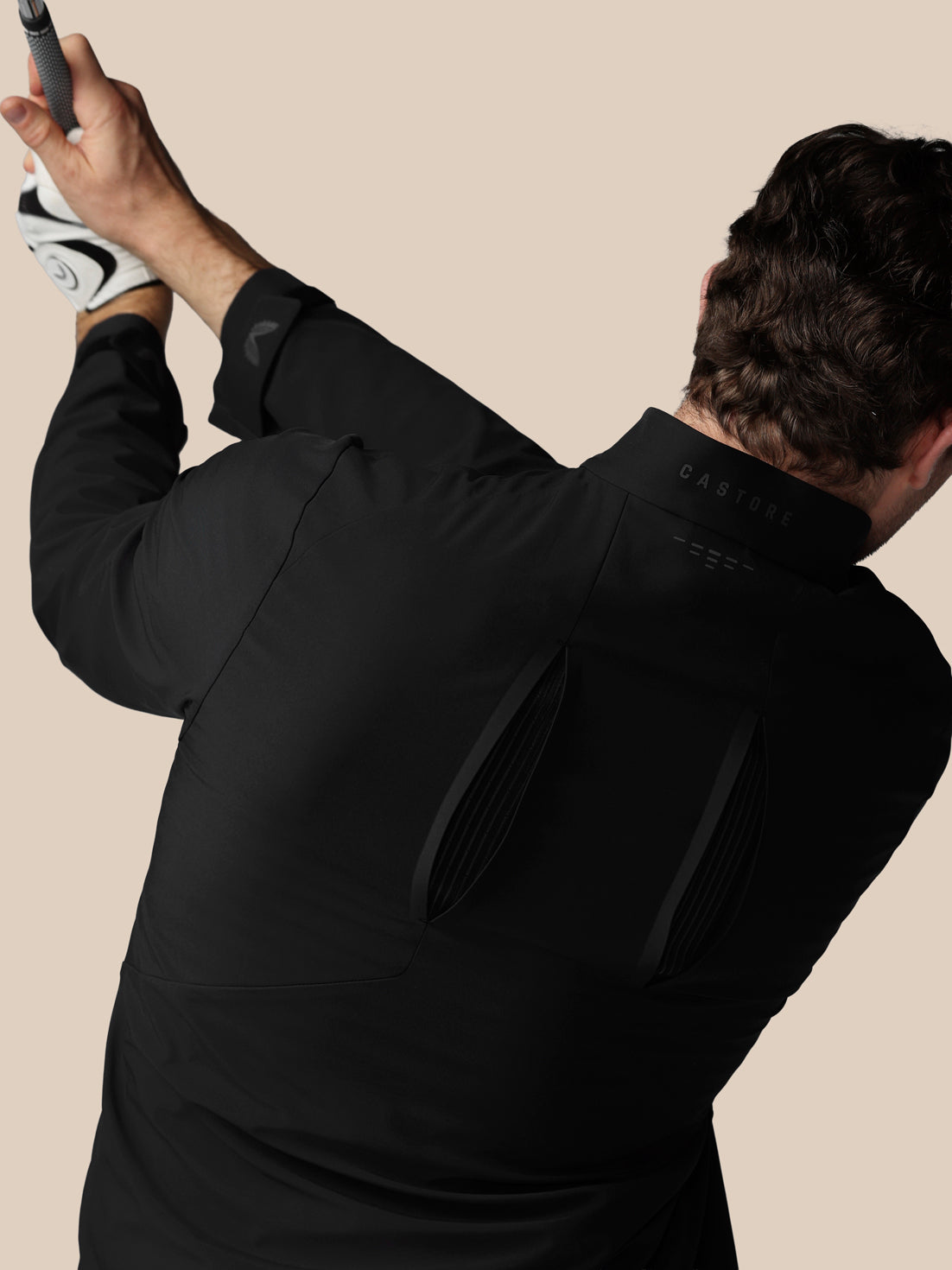 Man in a black suit holding a white object against a beige background