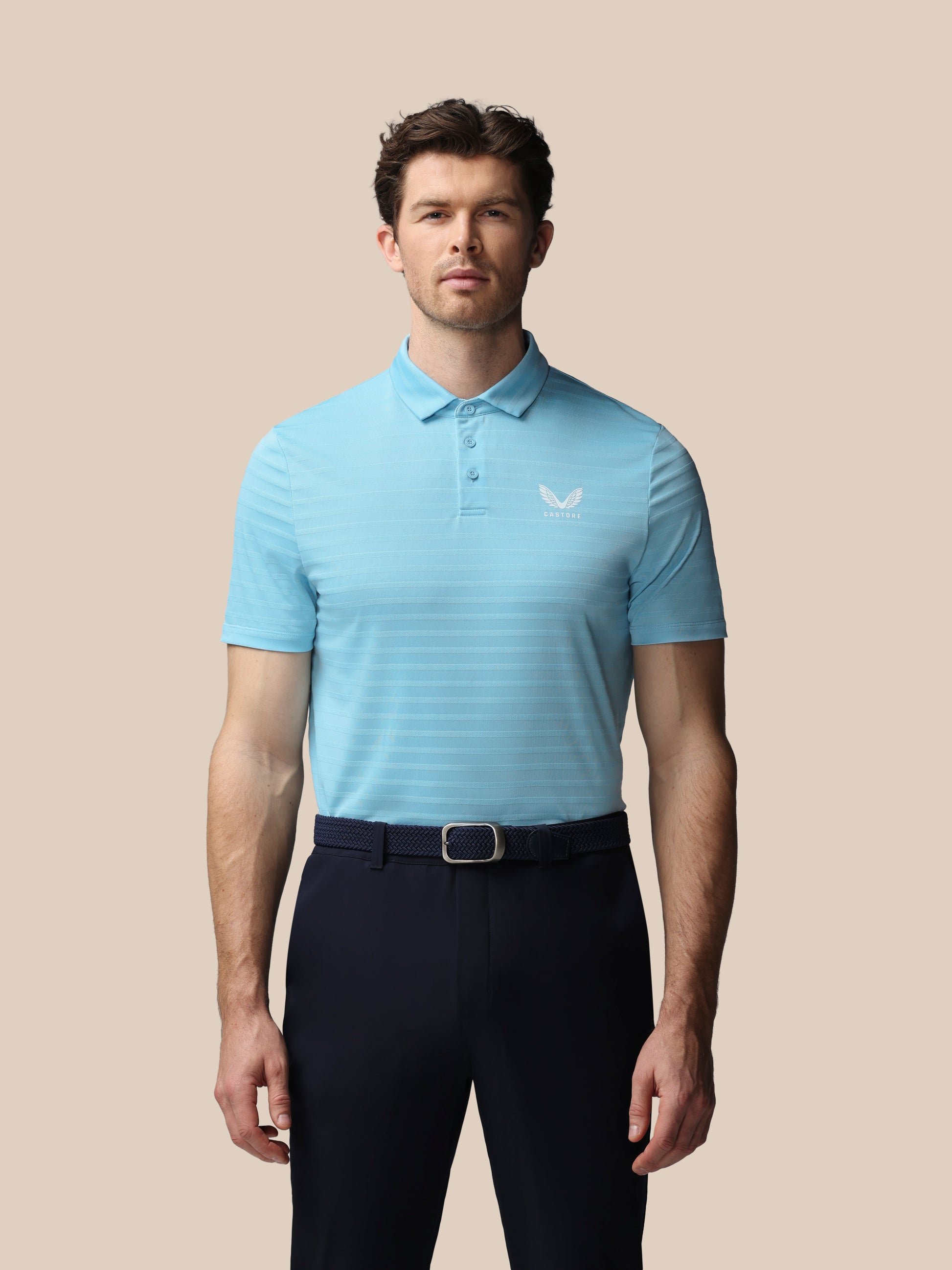 Man wearing a light blue striped polo shirt and dark pants on a beige background