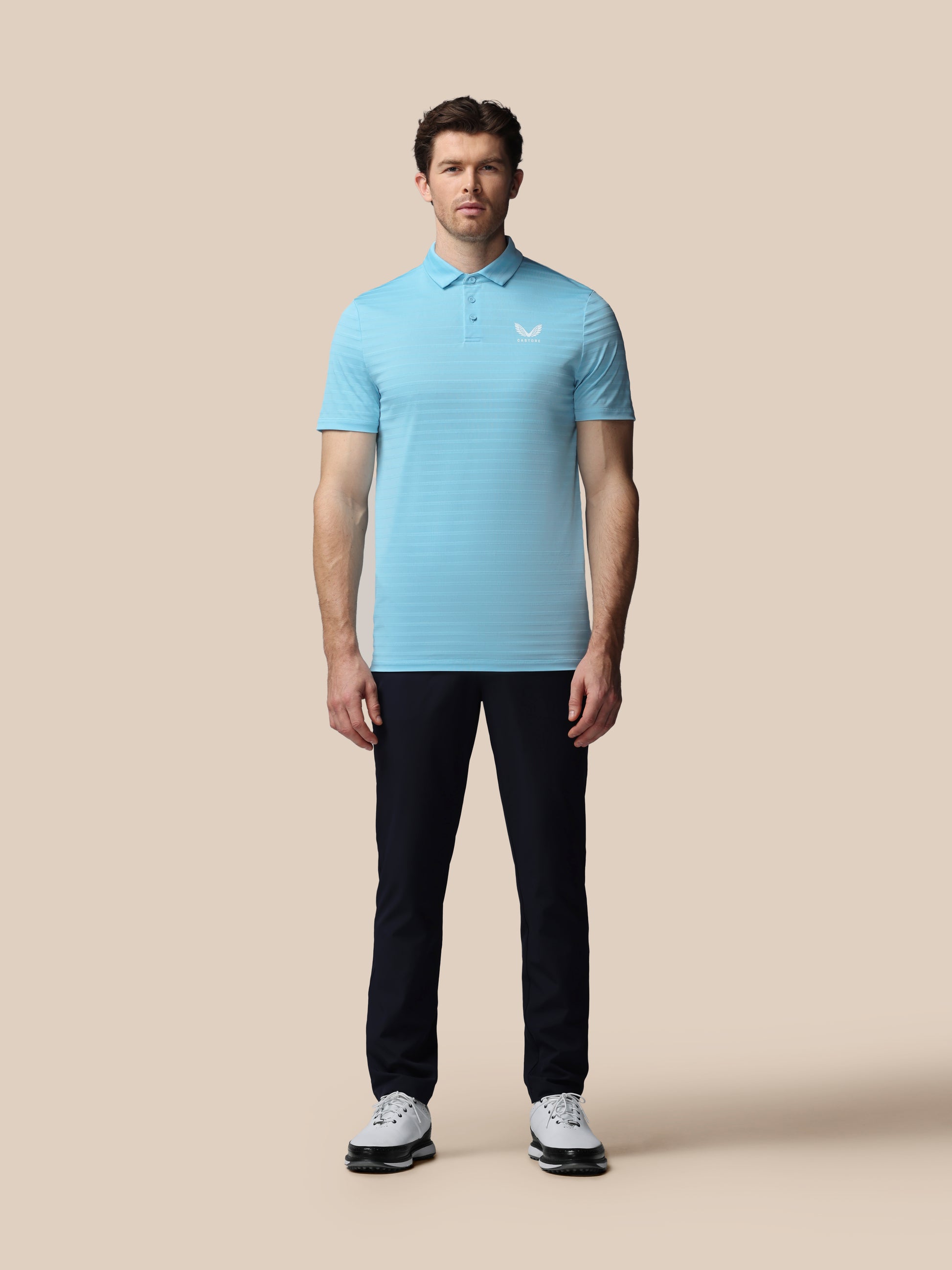 Man wearing a light blue striped polo shirt and dark pants on a beige background