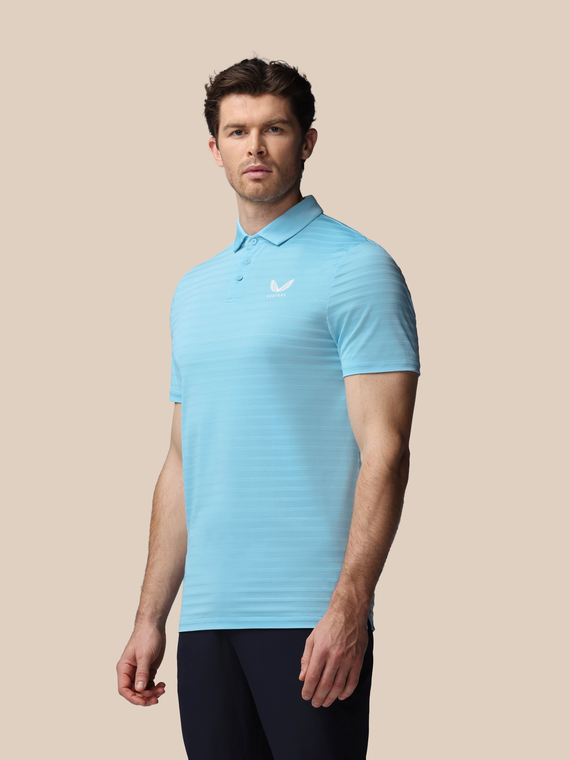 Man wearing a light blue polo shirt with a logo on a beige background