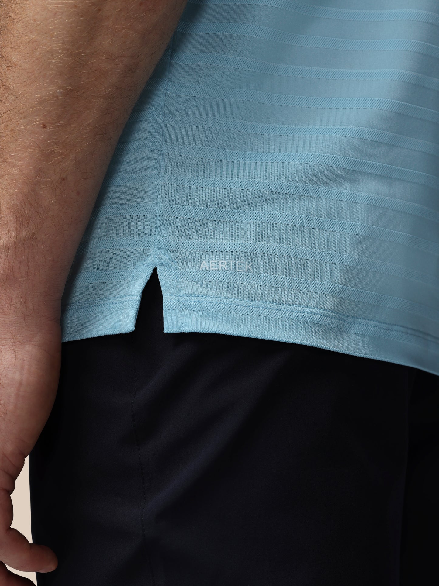 Close-up of a light blue shirt with 'AERTEK' branding on a person wearing black shorts.