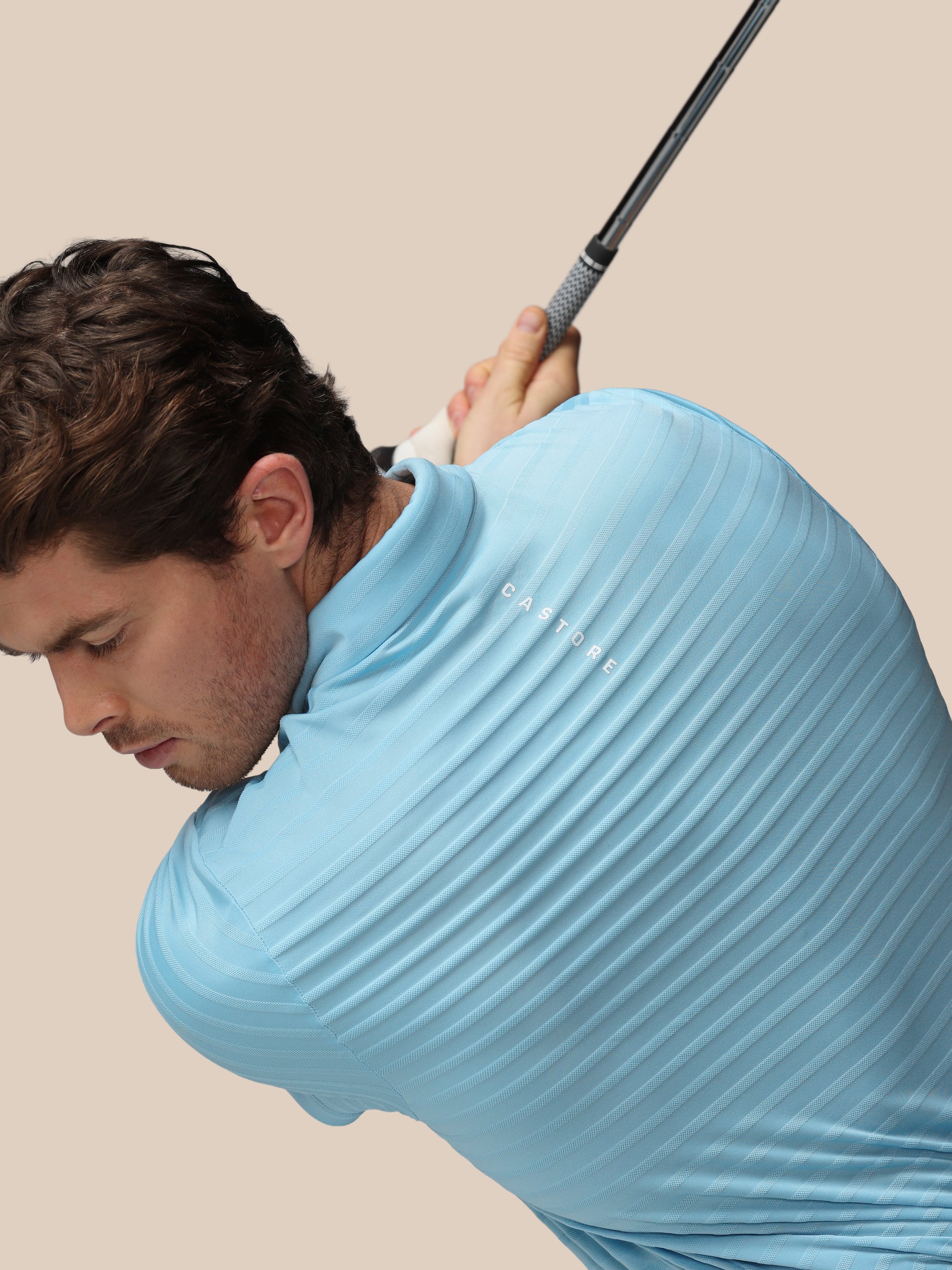 Man in a light blue shirt holding a golf club against a beige background