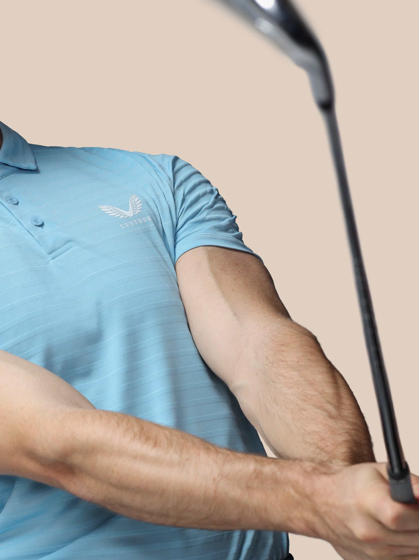 Person wearing a light blue polo shirt holding a golf club against a beige background