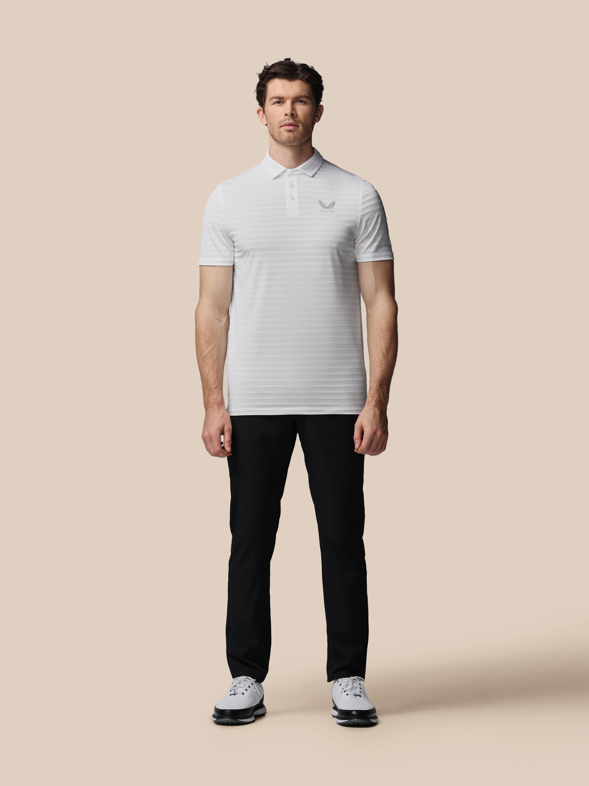 Man wearing a white polo shirt and black pants on a beige background