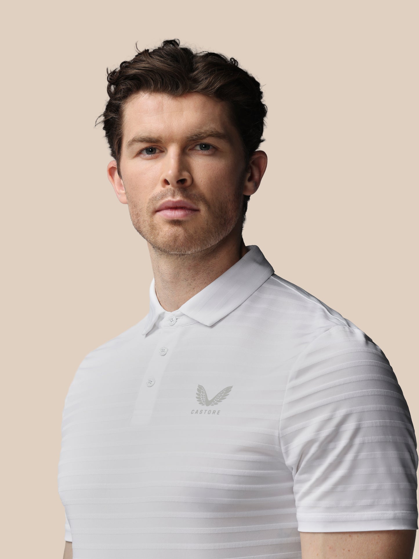 Man wearing a light gray polo shirt with a logo on a beige background
