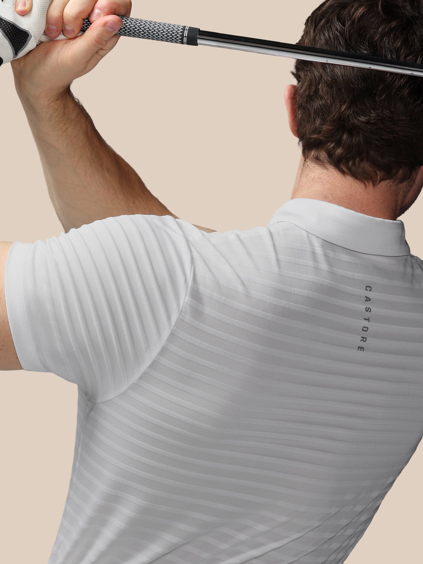 Person wearing a light gray polo shirt with a brand logo, holding a golf club.
