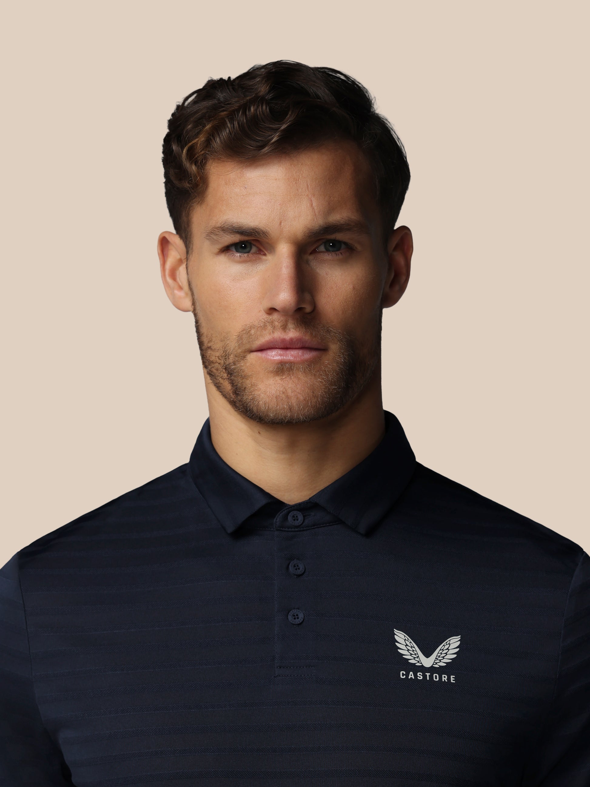 Man wearing a black polo shirt with a logo on a beige background