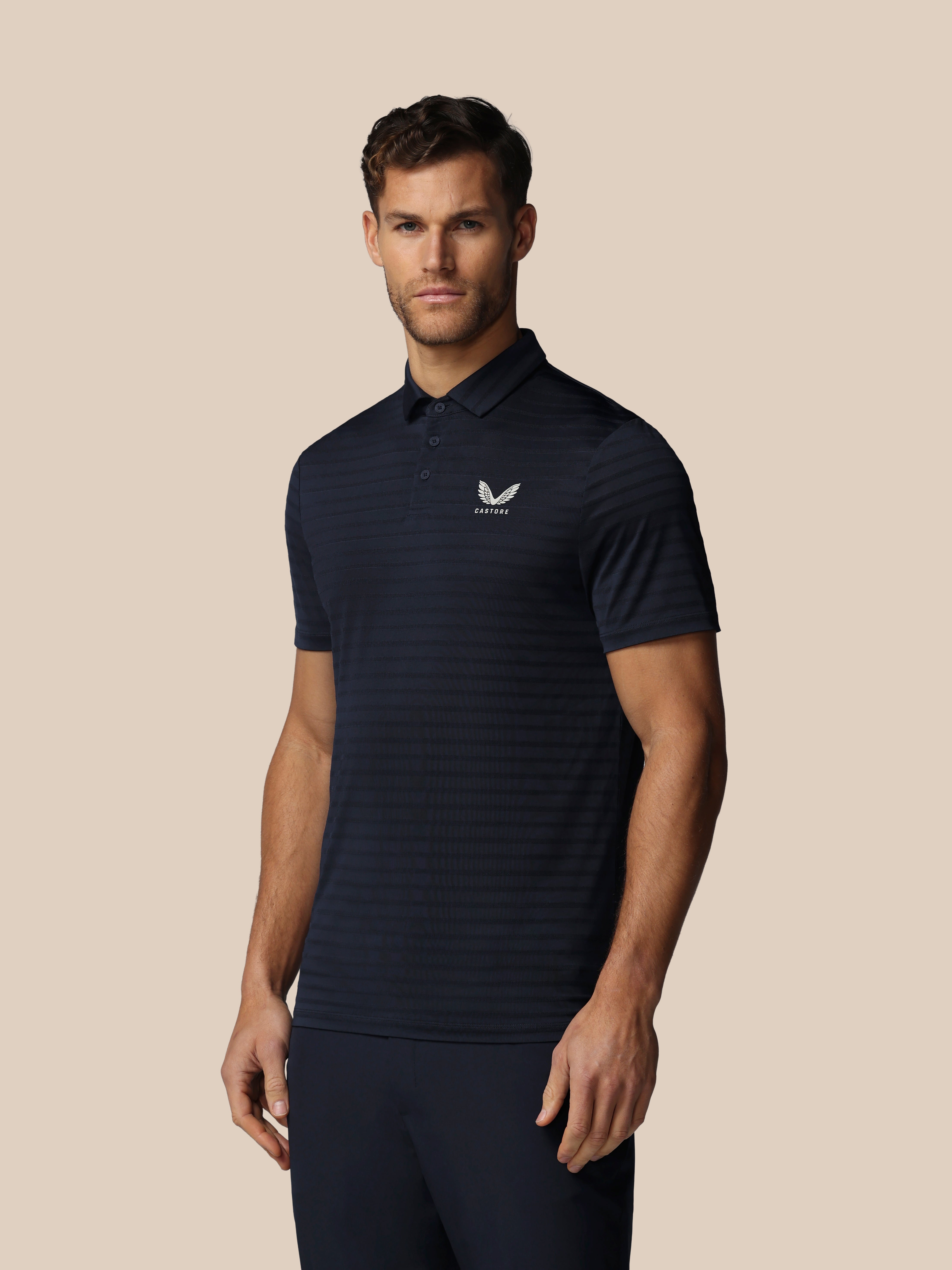 Man wearing a dark blue striped polo shirt with a logo on a beige background
