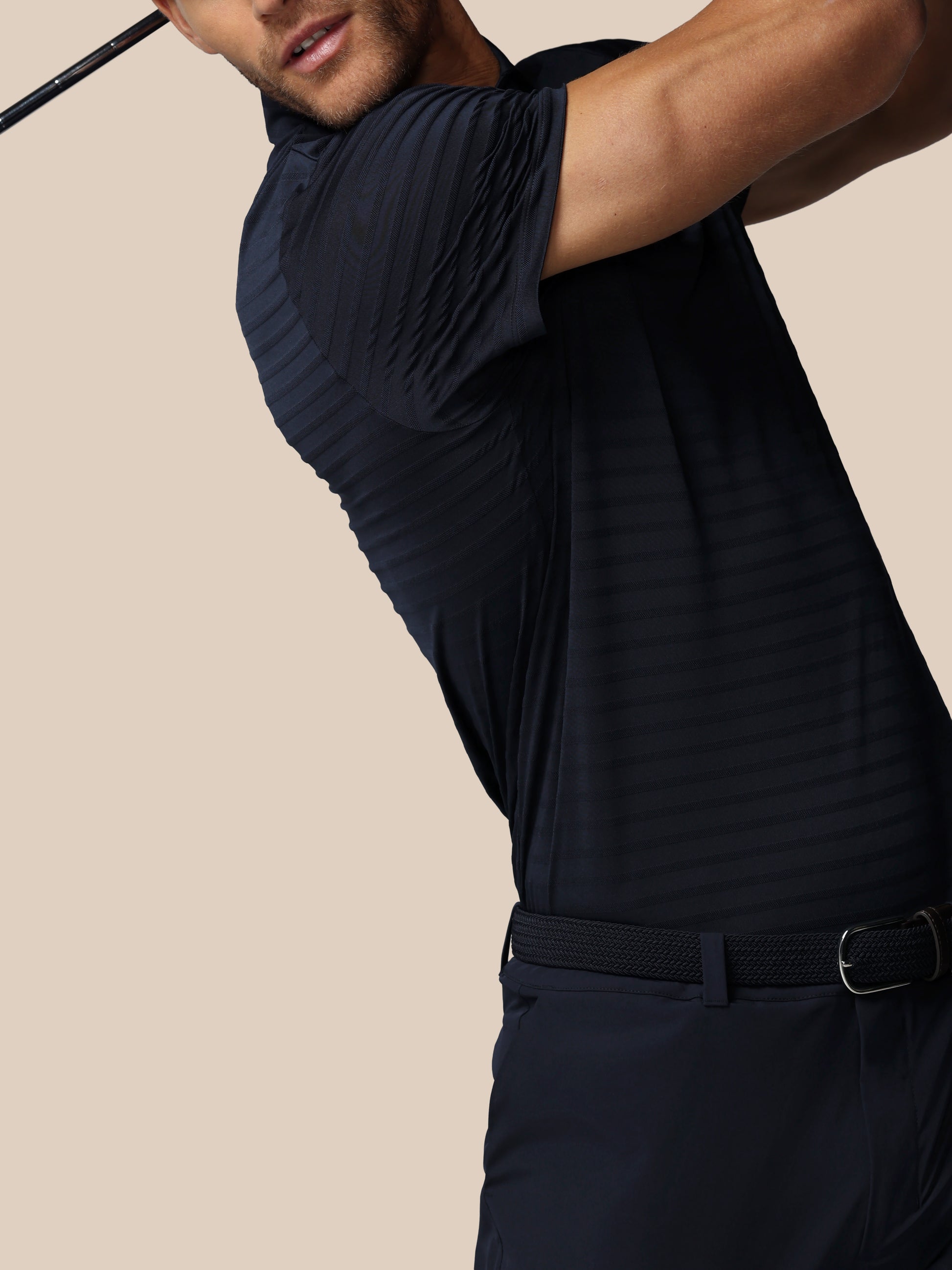 Man in a black outfit swinging a golf club against a beige background