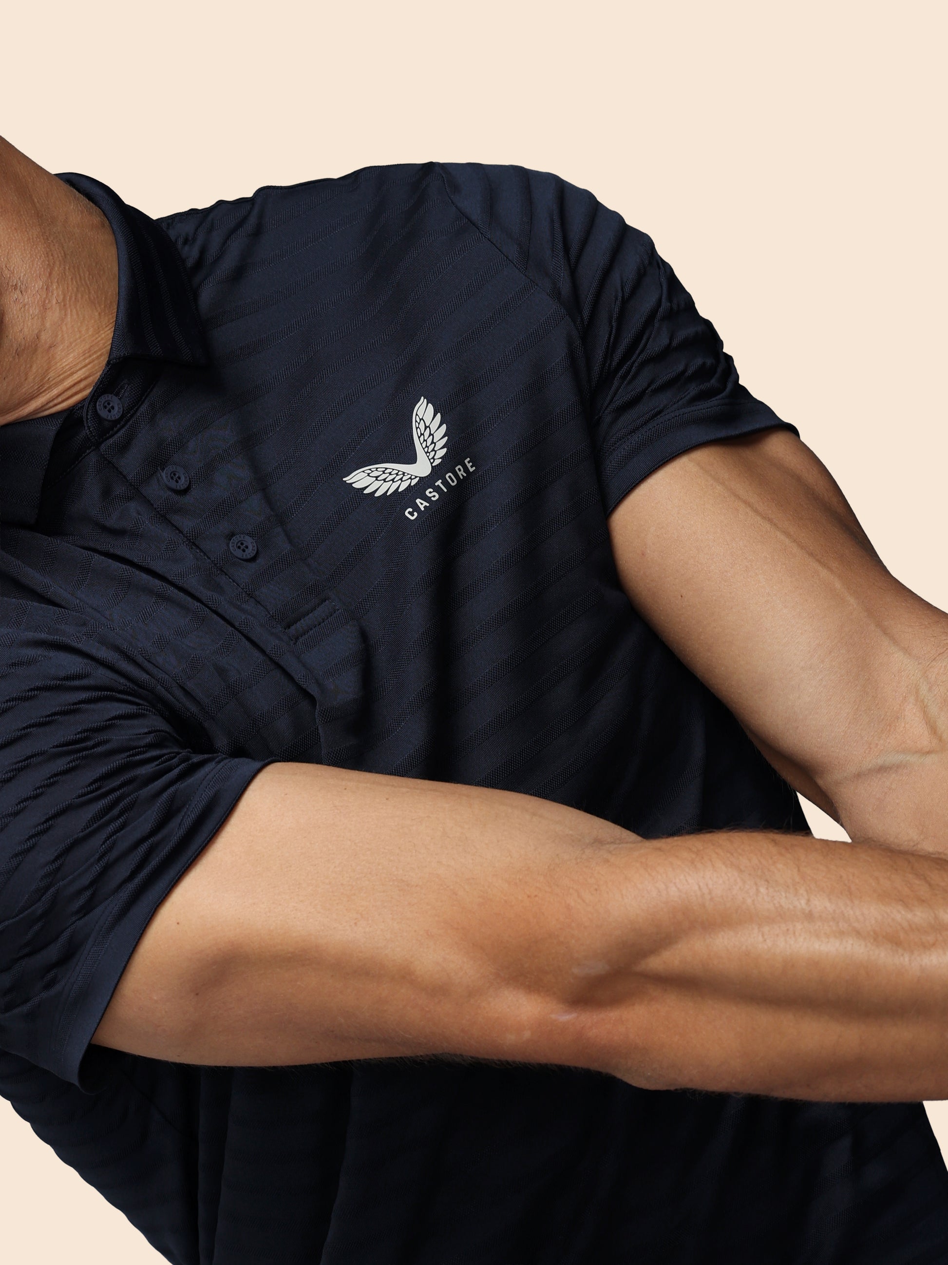 Person wearing a navy polo shirt with a logo on a beige background