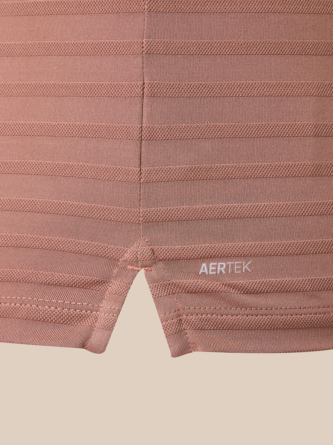 Close-up of ribbed knit athletic shorts in a dusty rose pink color, featuring horizontal compression stripes and a small white AERTEK logo near the hem.