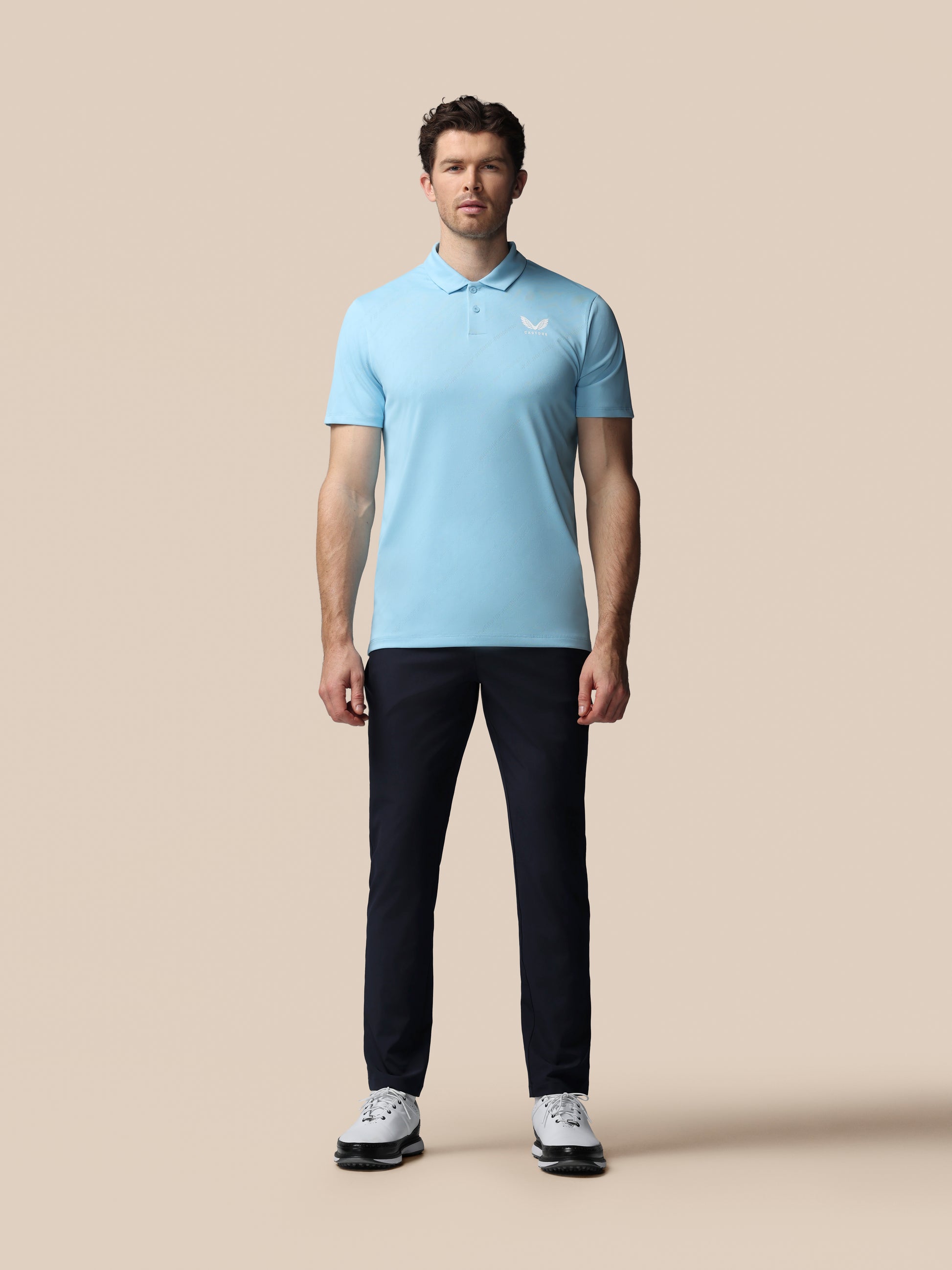 Man wearing a light blue polo shirt and black pants on a beige background