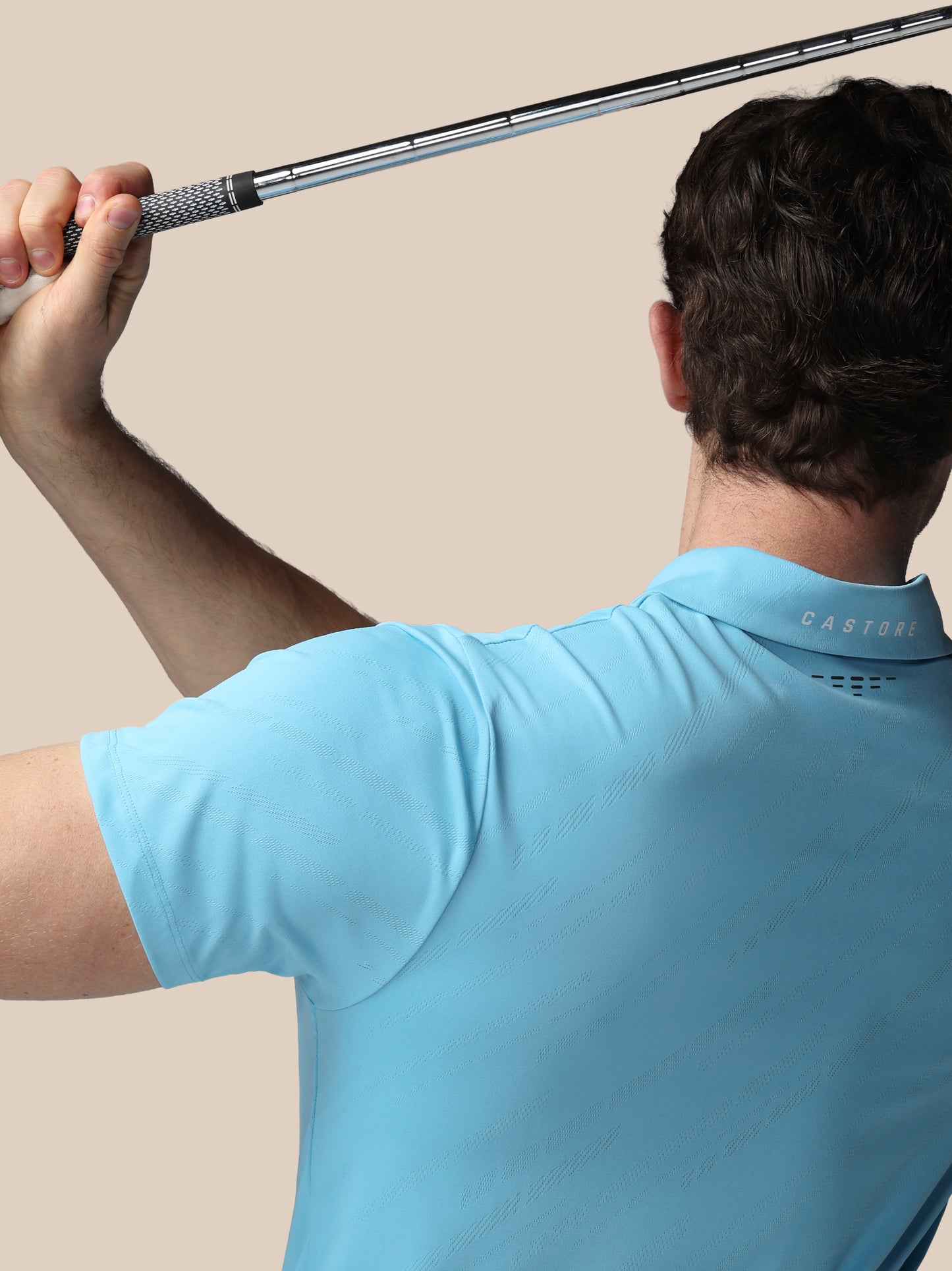 Person in a light blue shirt holding a golf club against a beige background