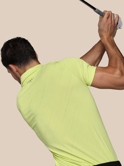 Man in a bright green shirt swinging a golf club against a beige background