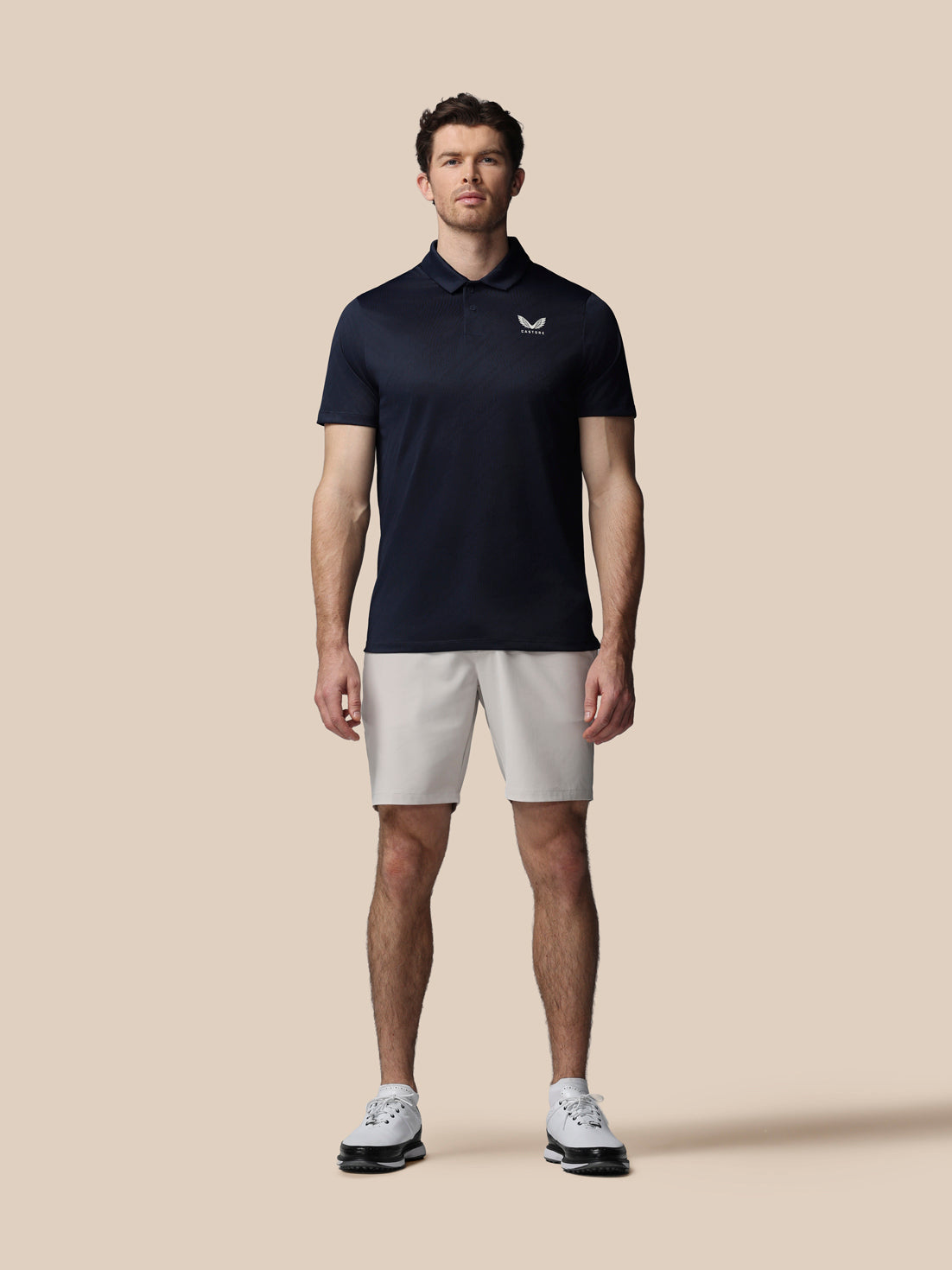 Man wearing a navy polo shirt and light gray shorts on a beige background