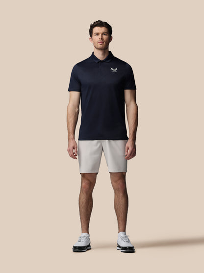 Man wearing a navy polo shirt and light gray shorts on a beige background