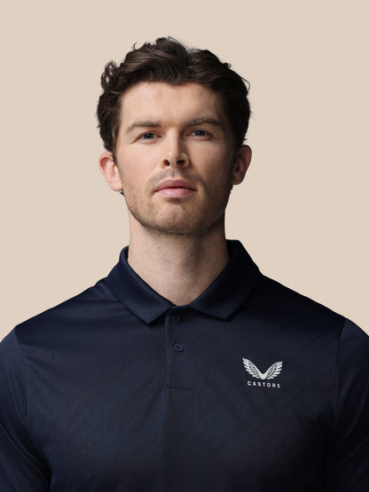Man wearing a navy polo shirt with a logo on a beige background