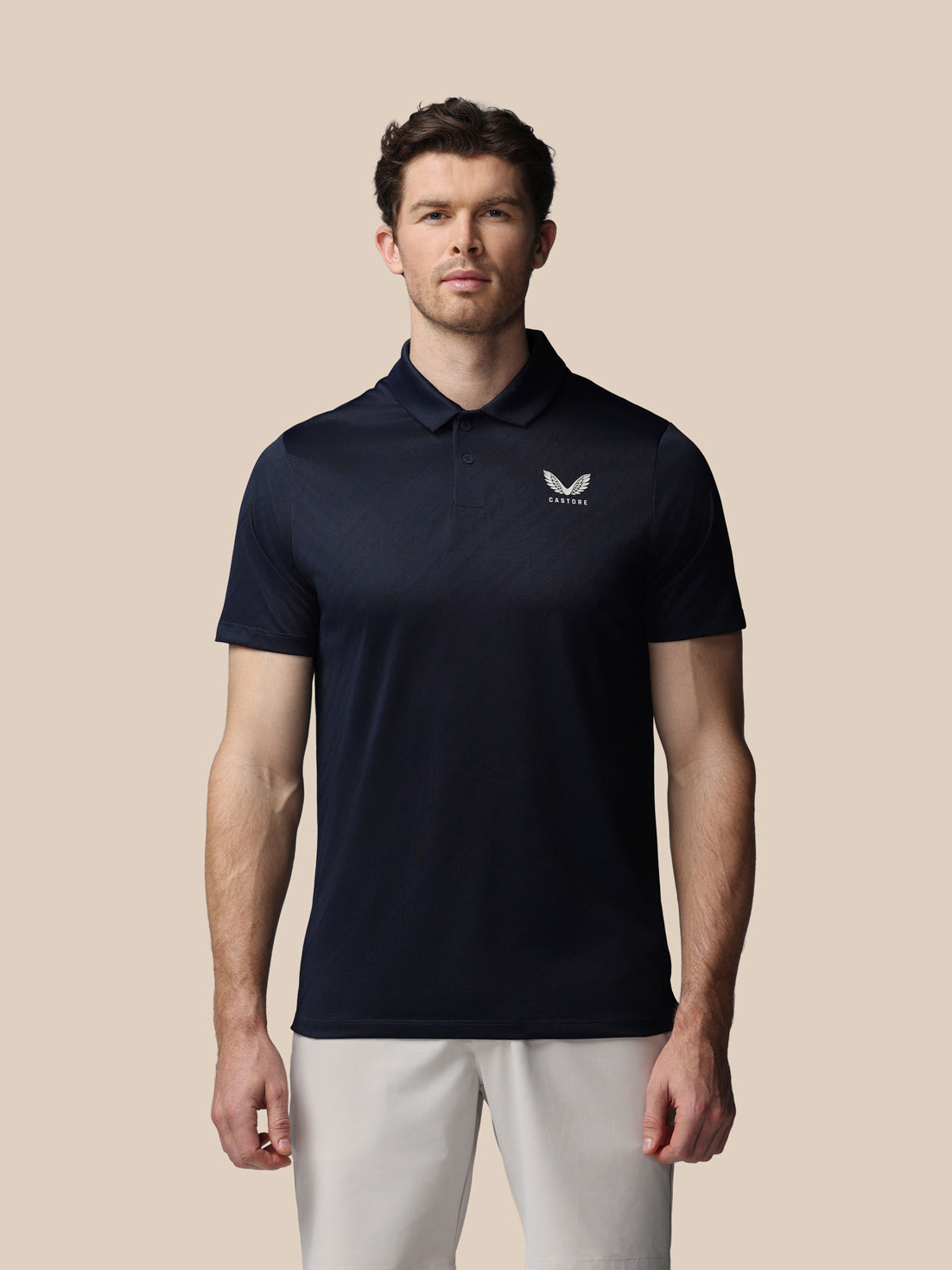 Man wearing a navy polo shirt with a logo on a beige background