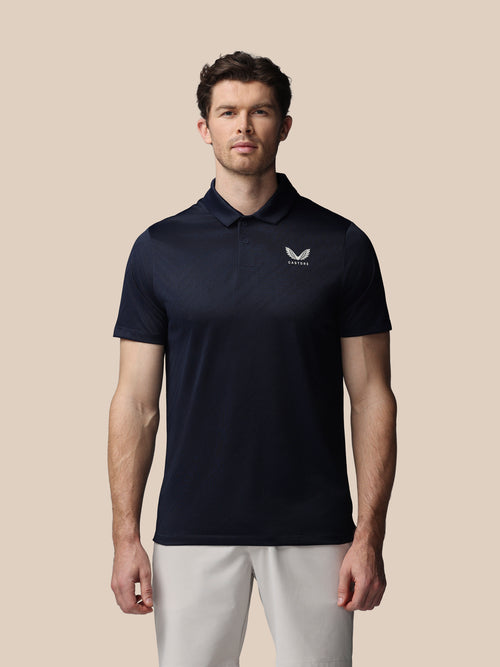 Man wearing a navy polo shirt with a logo on a beige background