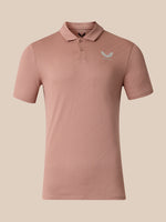 A short-sleeve polo shirt in a dusty rose pink color, featuring a small light gray wing logo on the left chest with the brand name 'Castore' underneath, displayed on a solid beige background.