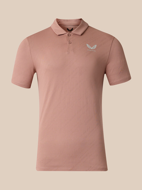 A short-sleeve polo shirt in a dusty rose pink color, featuring a small light gray wing logo on the left chest with the brand name 'Castore' underneath, displayed on a solid beige background.