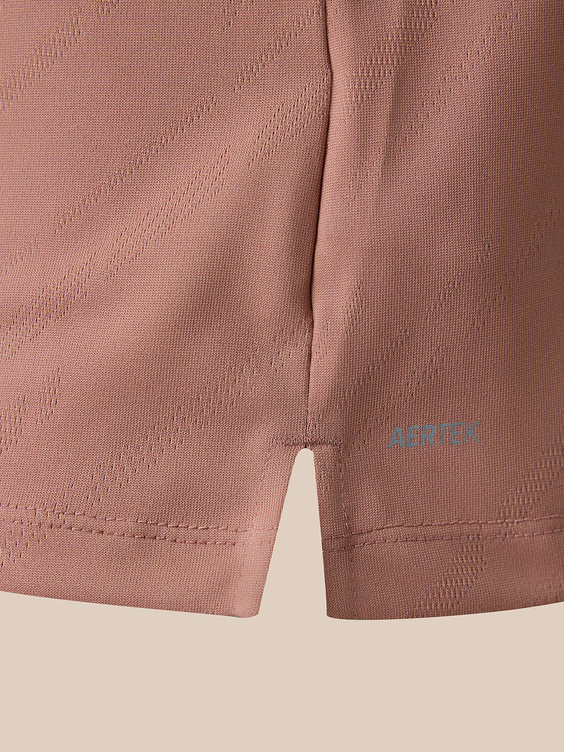 Close-up of a dusty rose athletic shorts leg showing the textured knit fabric, diagonal stitched pattern, and a small blue AERTEK logo near the hem.
