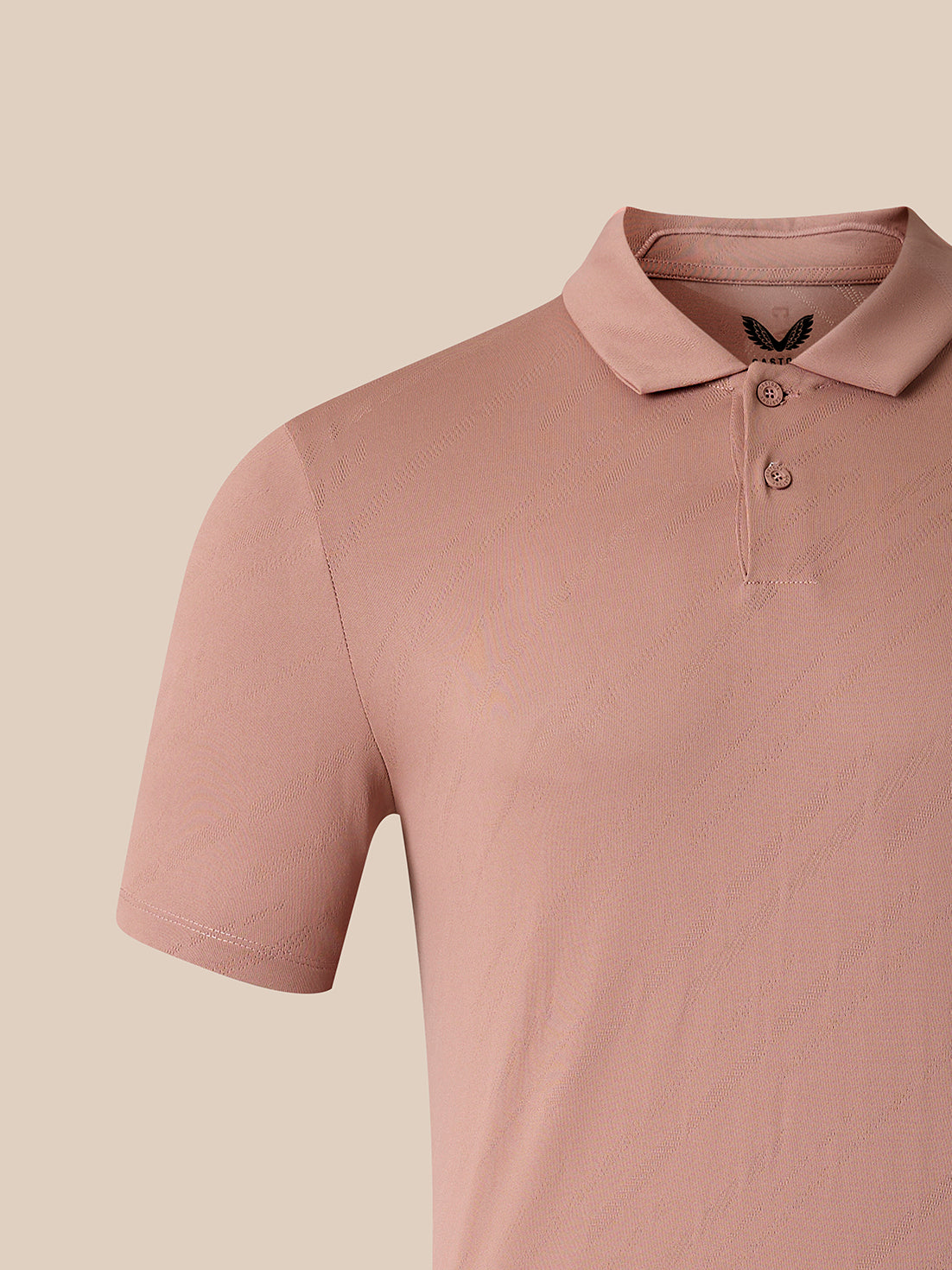 A close-up of a short-sleeve polo shirt in a dusty rose pink color, featuring a two-button placket and a small black embroidered bird logo on the inner neck label, set against a solid beige background.