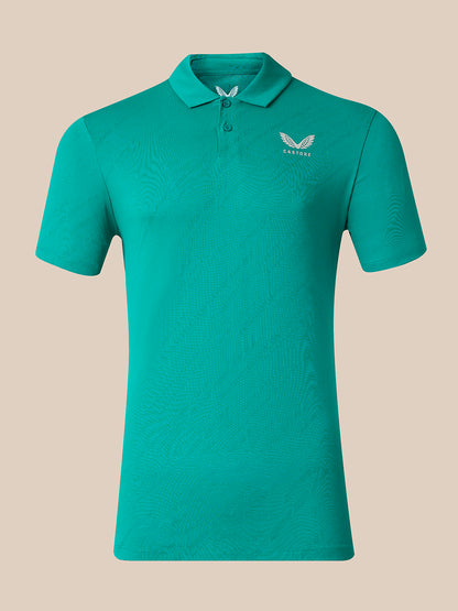 A short-sleeve polo shirt in a vibrant teal green color, featuring a subtle textured pattern and a small white wing logo with the brand name 'CASTORE' on the left chest, set against a solid beige background.