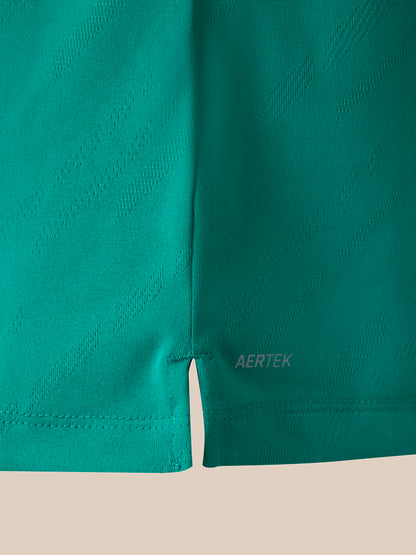 Close-up of teal athletic shirt showing the hem, stitched edge, and a small AERTEK logo near the lower right leg, set against a light beige background.