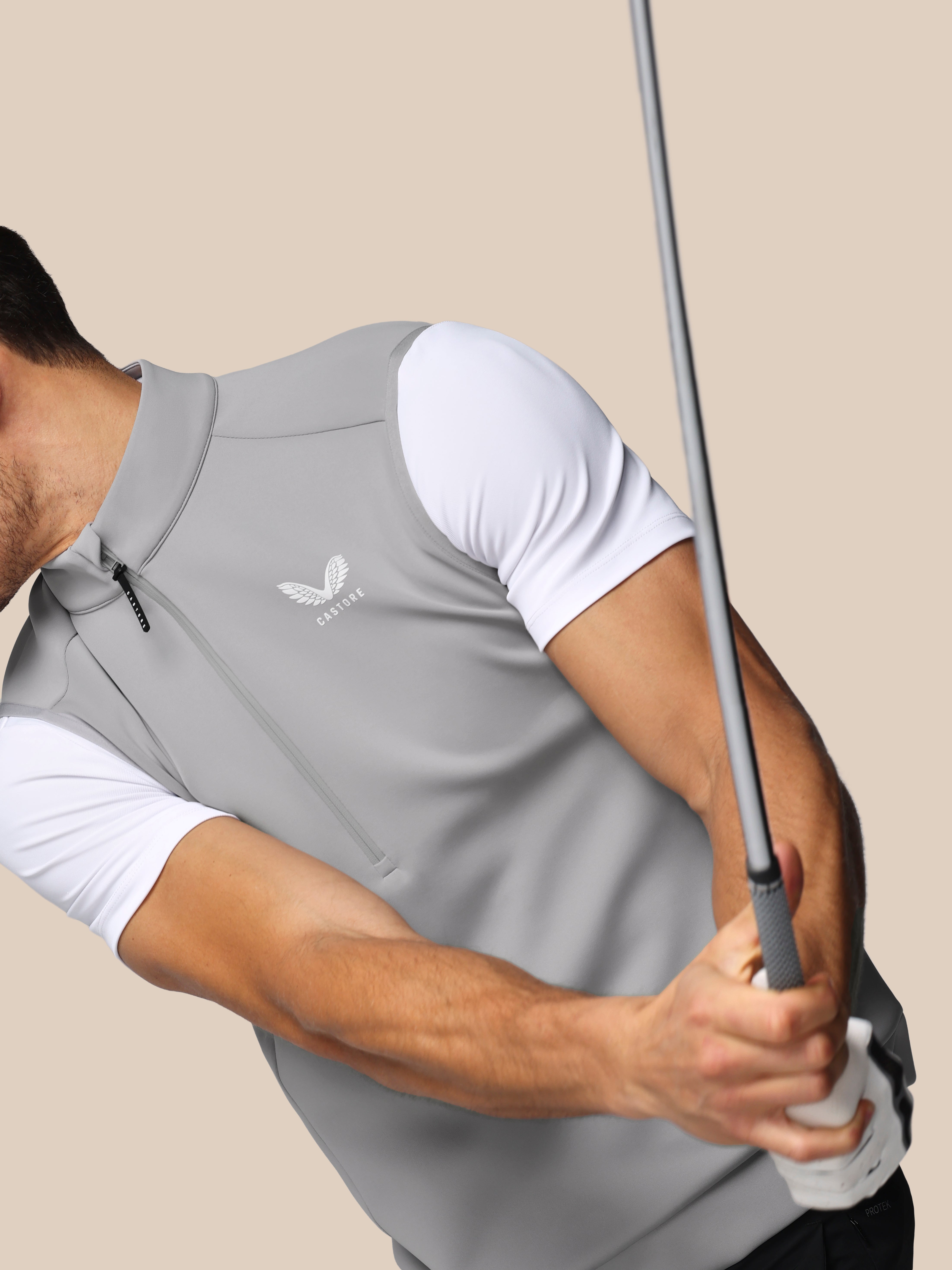 Person wearing a gray Castore shirt holding a golf club on a beige background