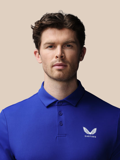 Man wearing a blue polo shirt with a logo on a beige background