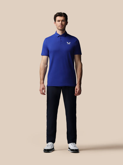 Man wearing a blue polo shirt and black pants on a beige background