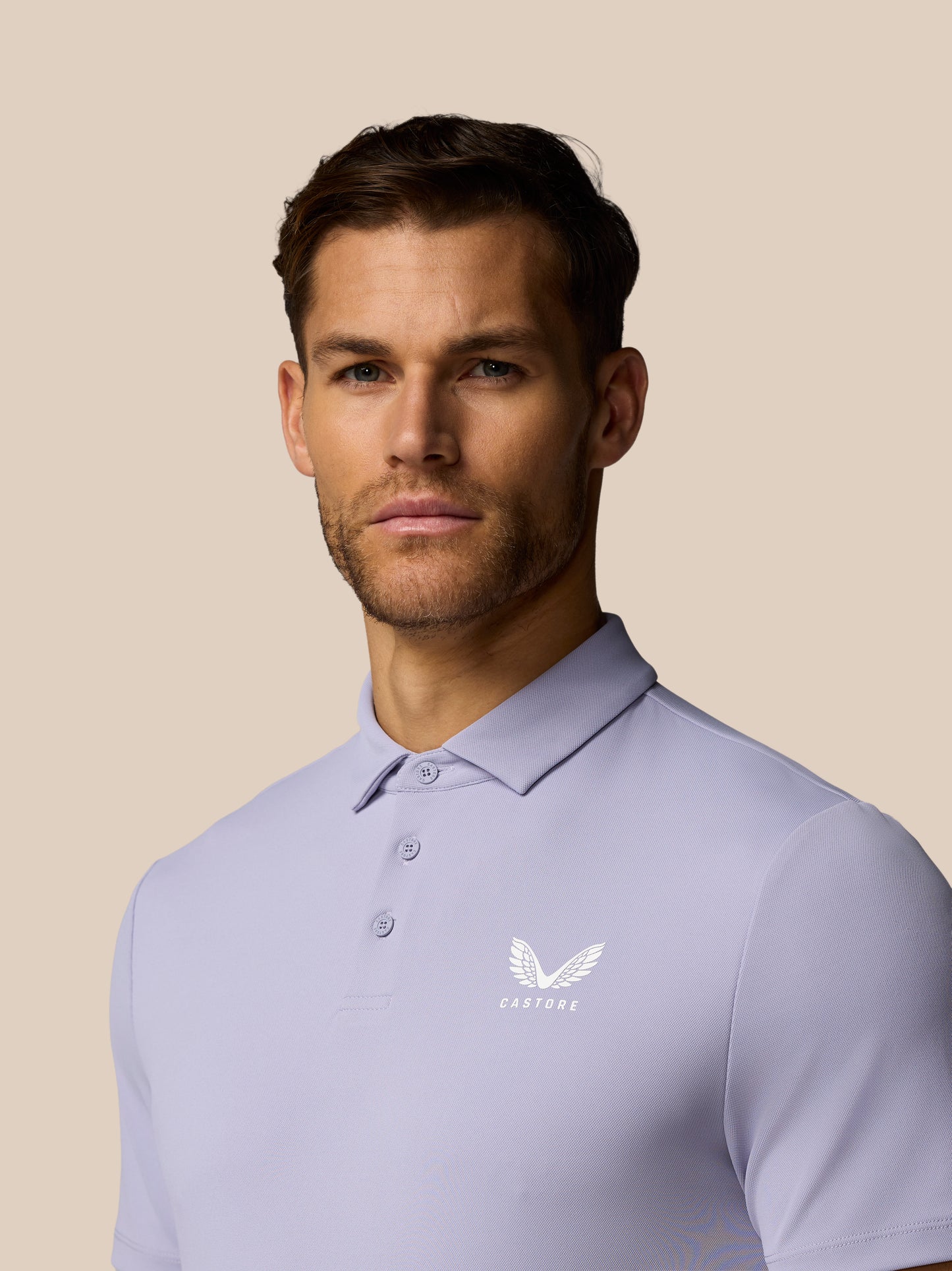 Man wearing a light purple polo shirt with a logo on a beige background