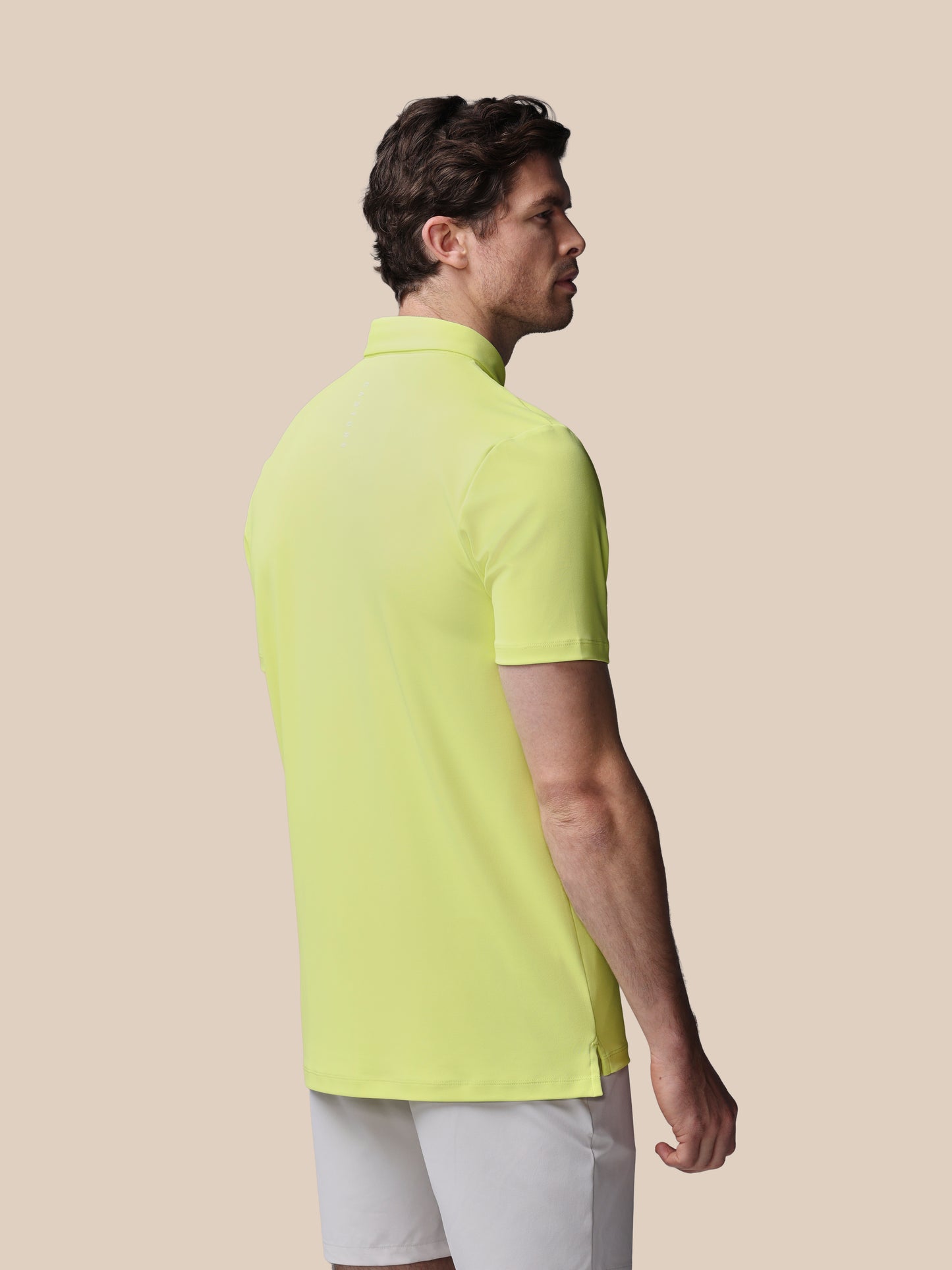 Man wearing a bright yellow polo shirt against a beige background