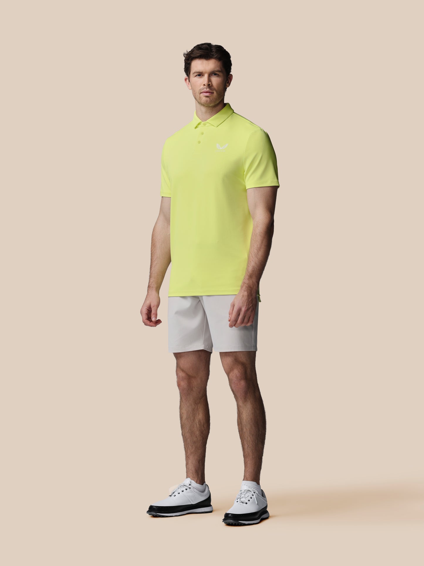 Man wearing a bright yellow polo shirt and white shorts on a beige background